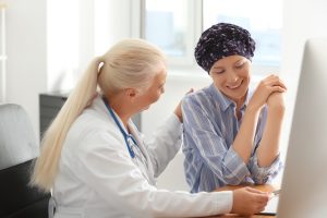 A doctor with a stethoscope talks to a smiling patient in a headscarf, offering support and discussing Wheaton cancer care packages in a bright medical office.