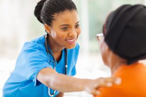 A nurse in blue scrubs with a stethoscope smiles and places a reassuring hand on the shoulder of a seated patient, highlighting the compassion found through Wheaton volunteer opportunities.