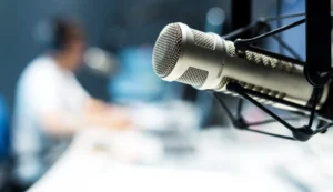 Close-up of a microphone in a recording studio, with a blurred person sitting at a desk in the background.