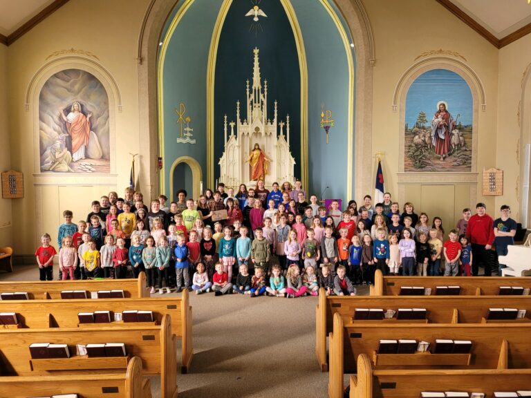 A large group of children and adults pose for a photo at the front of a church with wooden pews, religious murals, and an ornate altar in the background, gathering to support Chicago faith-based cancer support initiatives.
