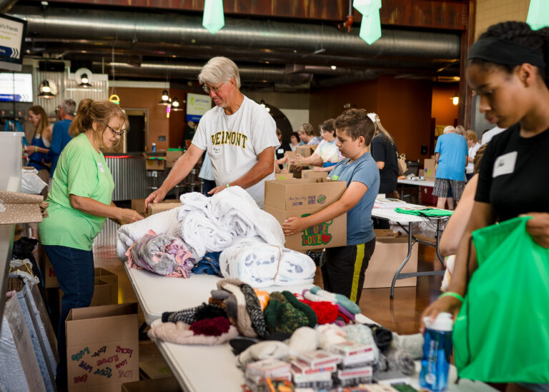 Volunteers sort and pack donated items, such as towels, scarves, and toiletries, on tables in a community center as part of Wheaton volunteer opportunities.