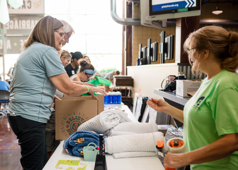 Several people distribute and organize donated supplies, including towels, bottles, and clothes, at an indoor event where Indianapolis donations help support those in need.