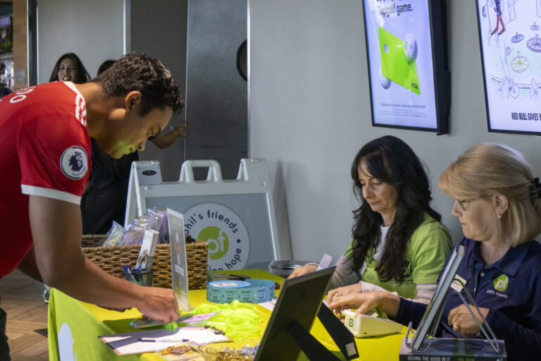 A man fills out a form at an event registration table staffed by two women, with informational materials about Chicago faith-based cancer support and raffle tickets on the table.