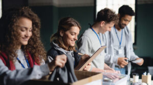 Four people sort and organize donations at a table, with boxes labeled "donations," clipboards, and various items being sorted.
