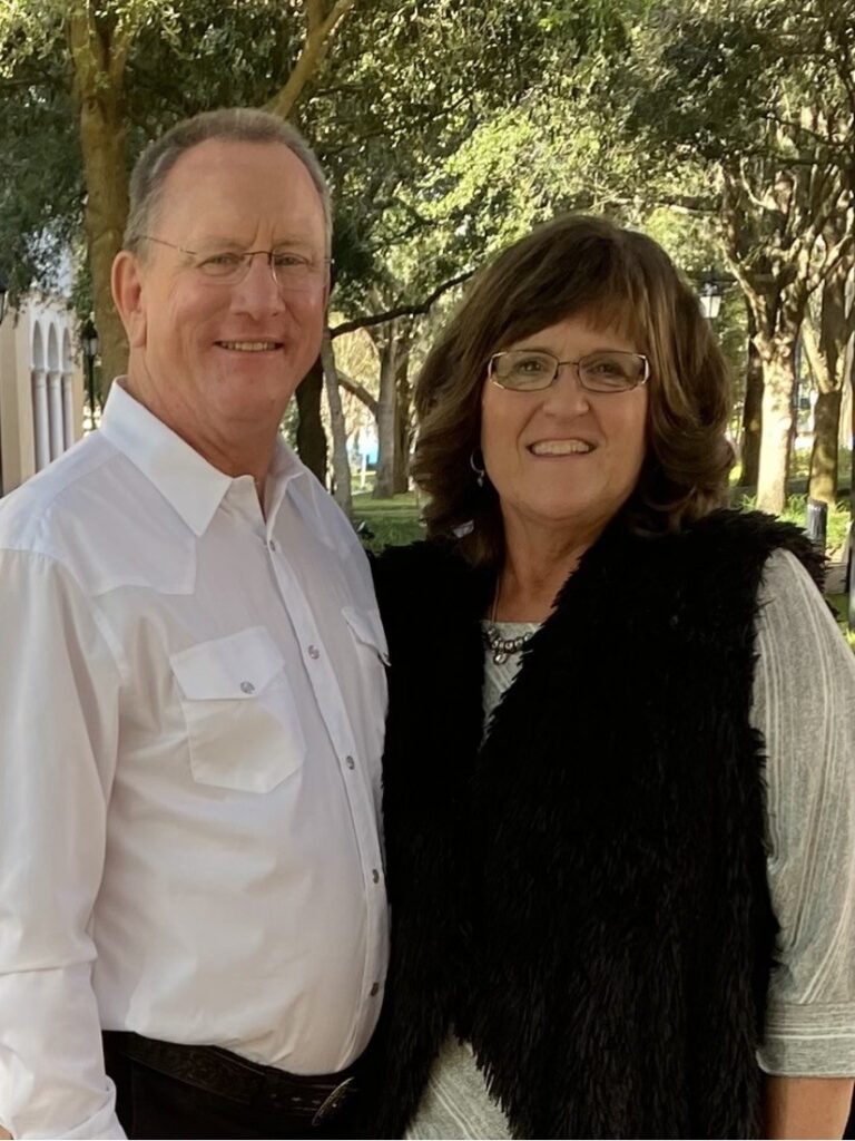 A middle-aged man in a white button-down shirt and a woman in a black vest standing together outdoors.