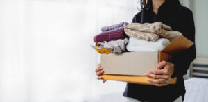 A person holding a cardboard box filled with folded clothes.